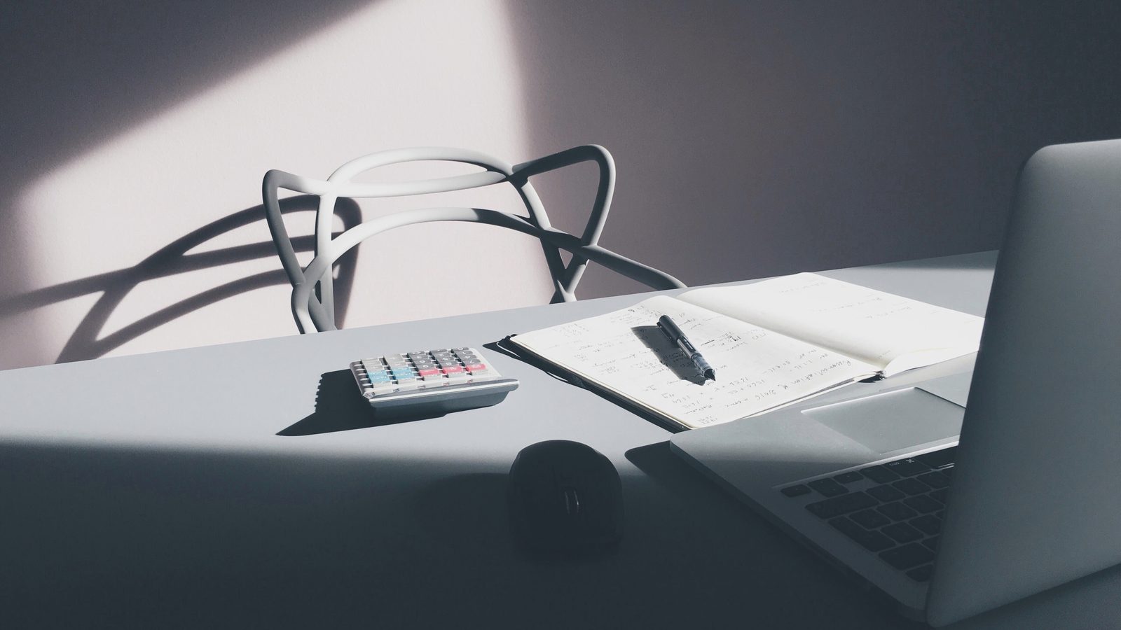 Una scrivania con un portatile, una calcolatrice e un blocco di appunti